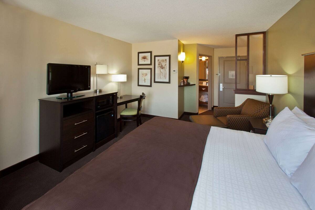 Ein Hotelzimmer mit einem Bett, einem Schreibtisch, einem Fernseher, einem Sessel, einer Couch und einem Schrank.