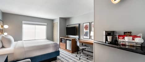 A hotel room with a bed, desk, TV, and a minibar.