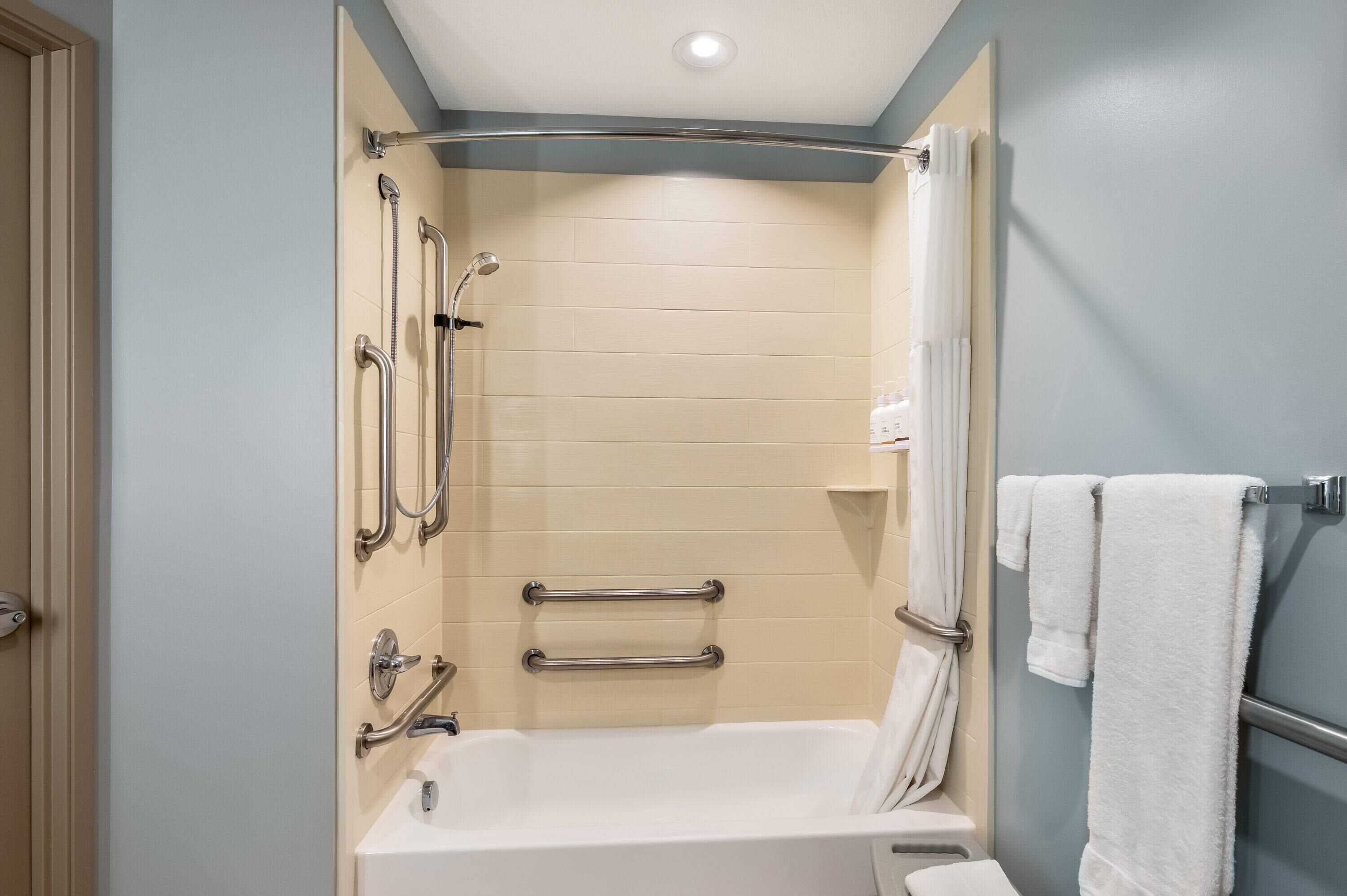 A bathroom with a bathtub, grab bars, a showerhead, and a towel rack.