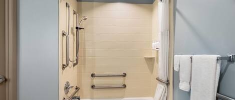 A bathroom with a bathtub, grab bars, a showerhead, and a towel rack.