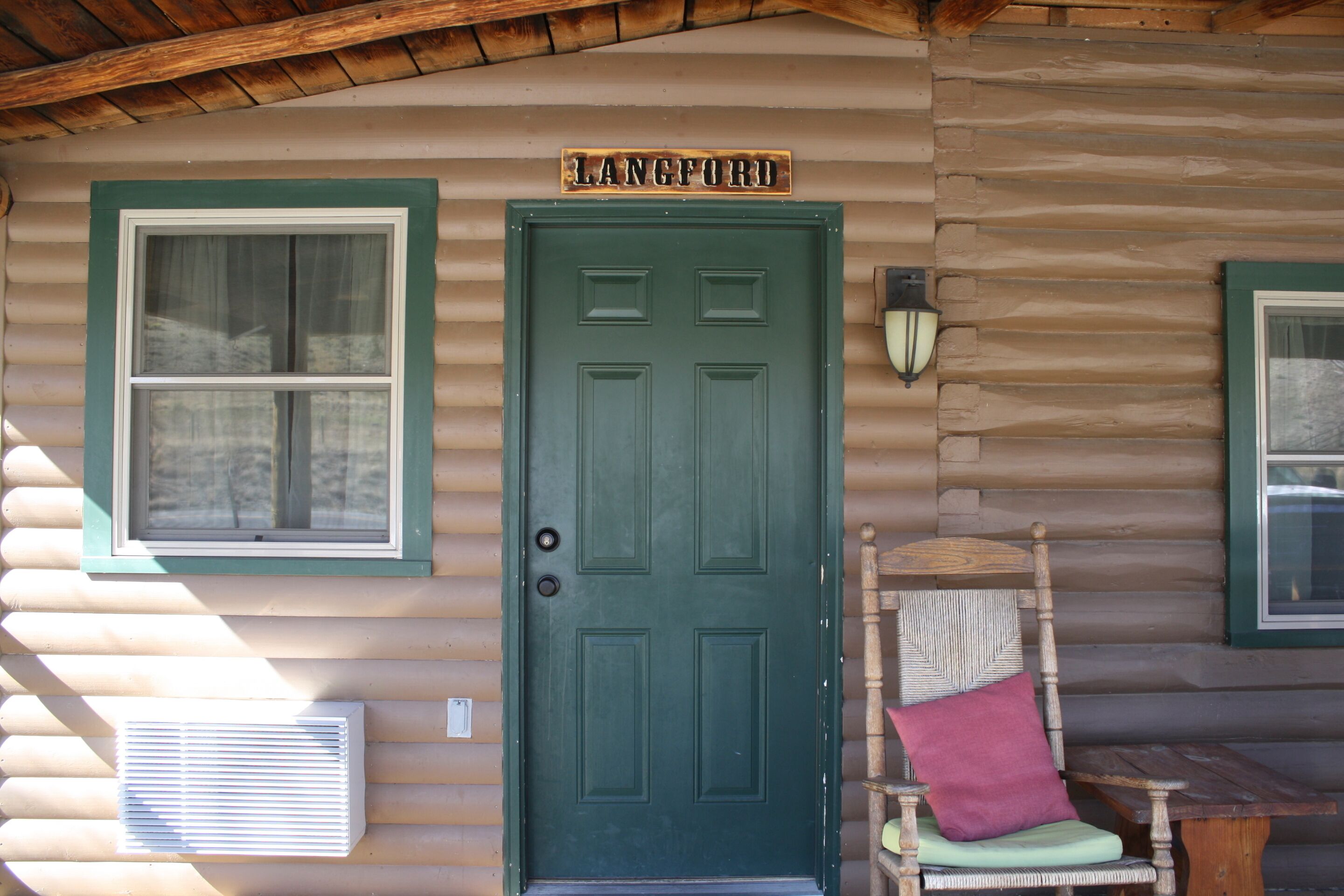 A log cabin with a green door, a window with a white frame, and a sign above the door that reads "LANGFORD".