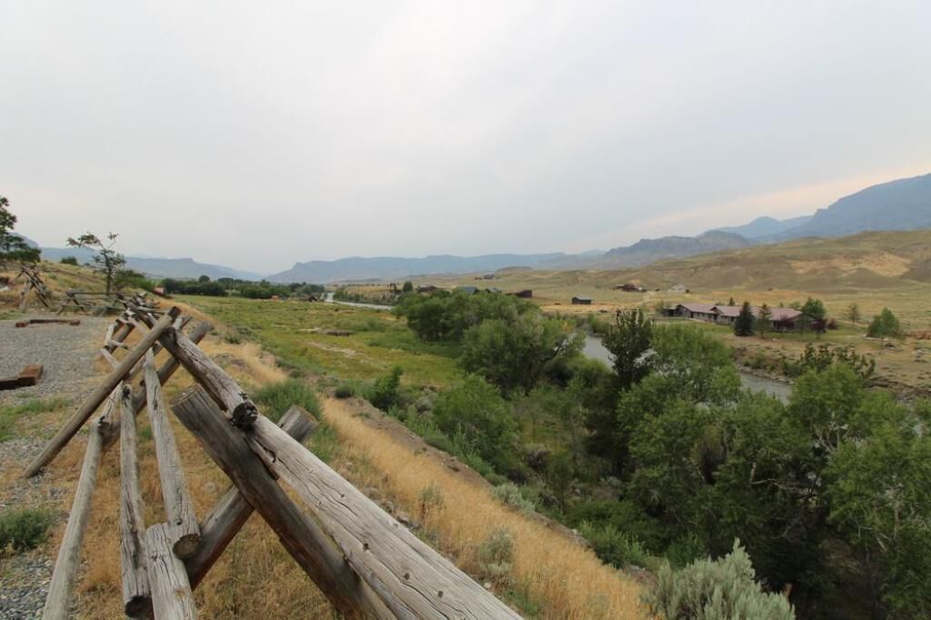 A rural landscape with a wooden fence, a small stream, and scattered buildings in the distance.