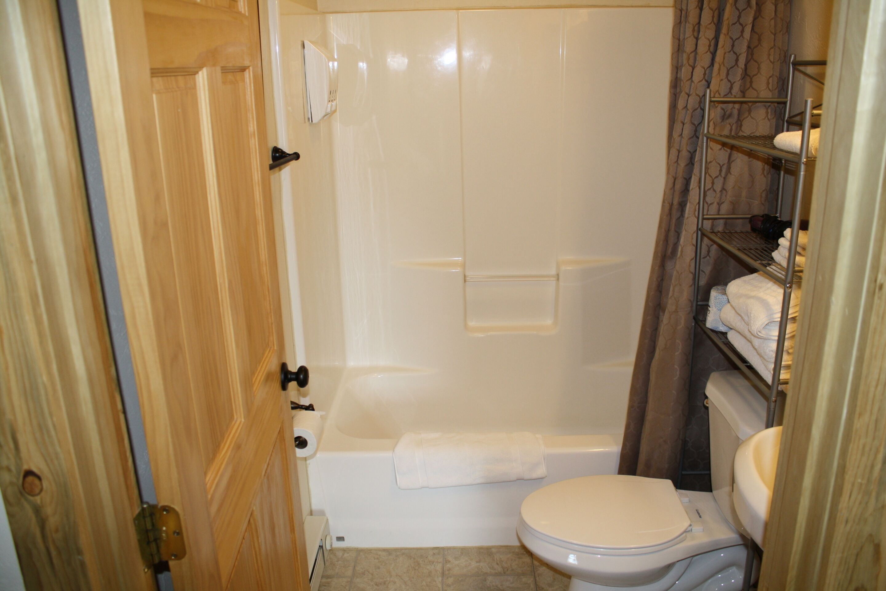 A bathroom with a bathtub, toilet, and a shelf with towels.