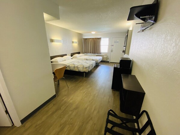 A hotel room with two single beds, a desk, a chair, a TV, and a door.