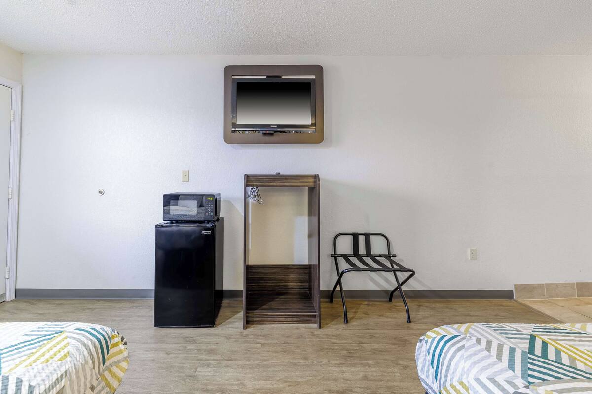 A hotel room with two beds, a desk with a computer, a TV mounted on the wall, and a chair.