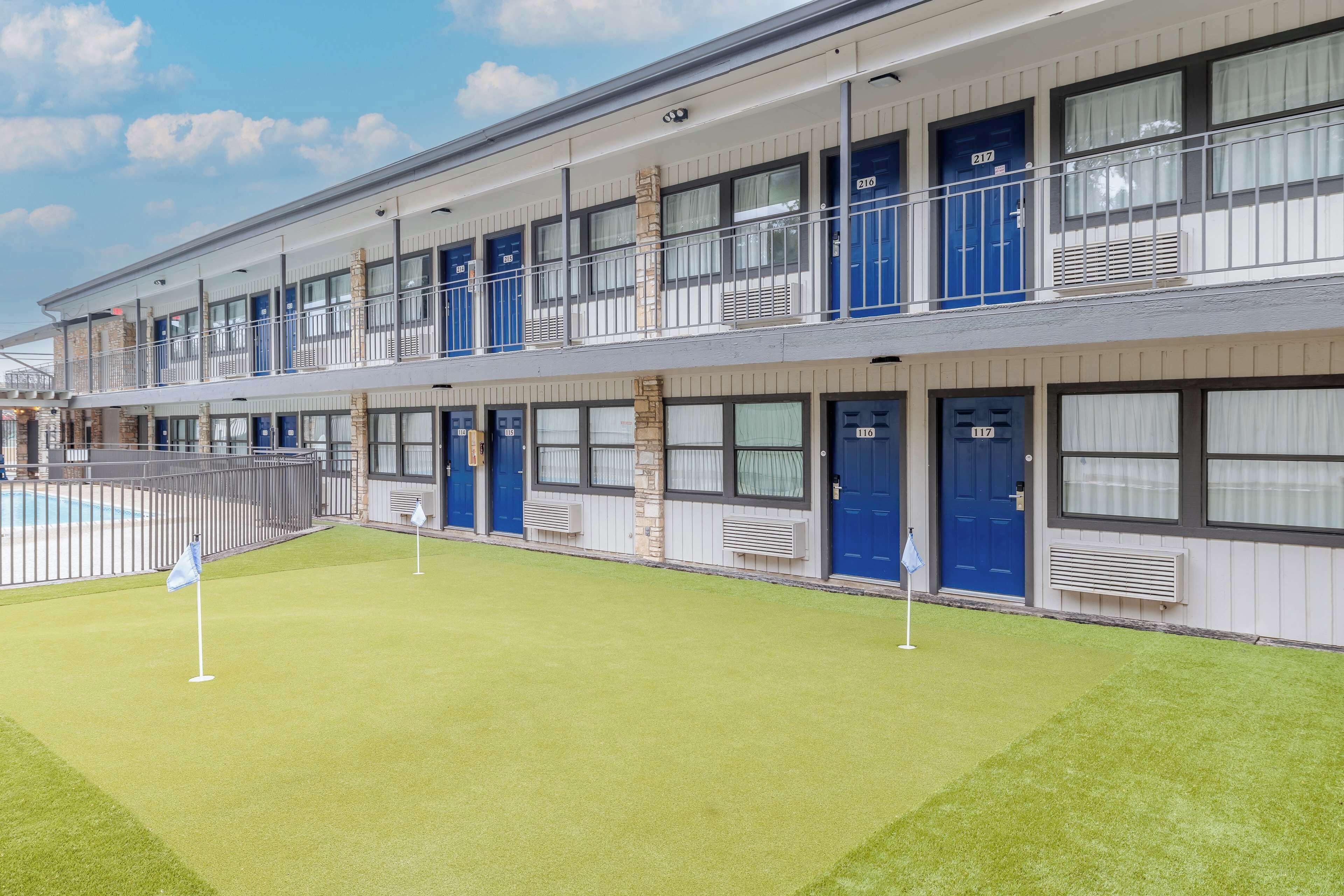 A multi-story hotel with individual rooms on each floor, a swimming pool, and a well-maintained lawn.