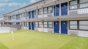 A multi-story hotel with individual rooms on each floor, a swimming pool, and a well-maintained lawn.