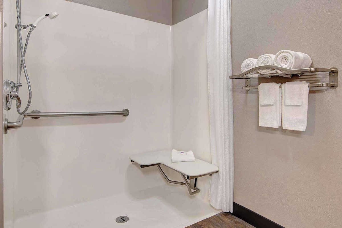 A shower with a grab bar, a small bench, and a towel rack with towels.