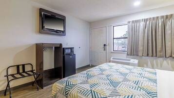 A hotel room with a bed, a TV mounted on the wall, a desk with a microwave, and a window with curtains.