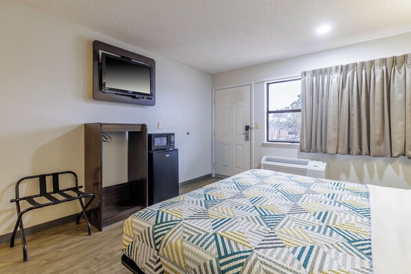 A hotel room with a bed, a television, a refrigerator, a desk, and a window with curtains.