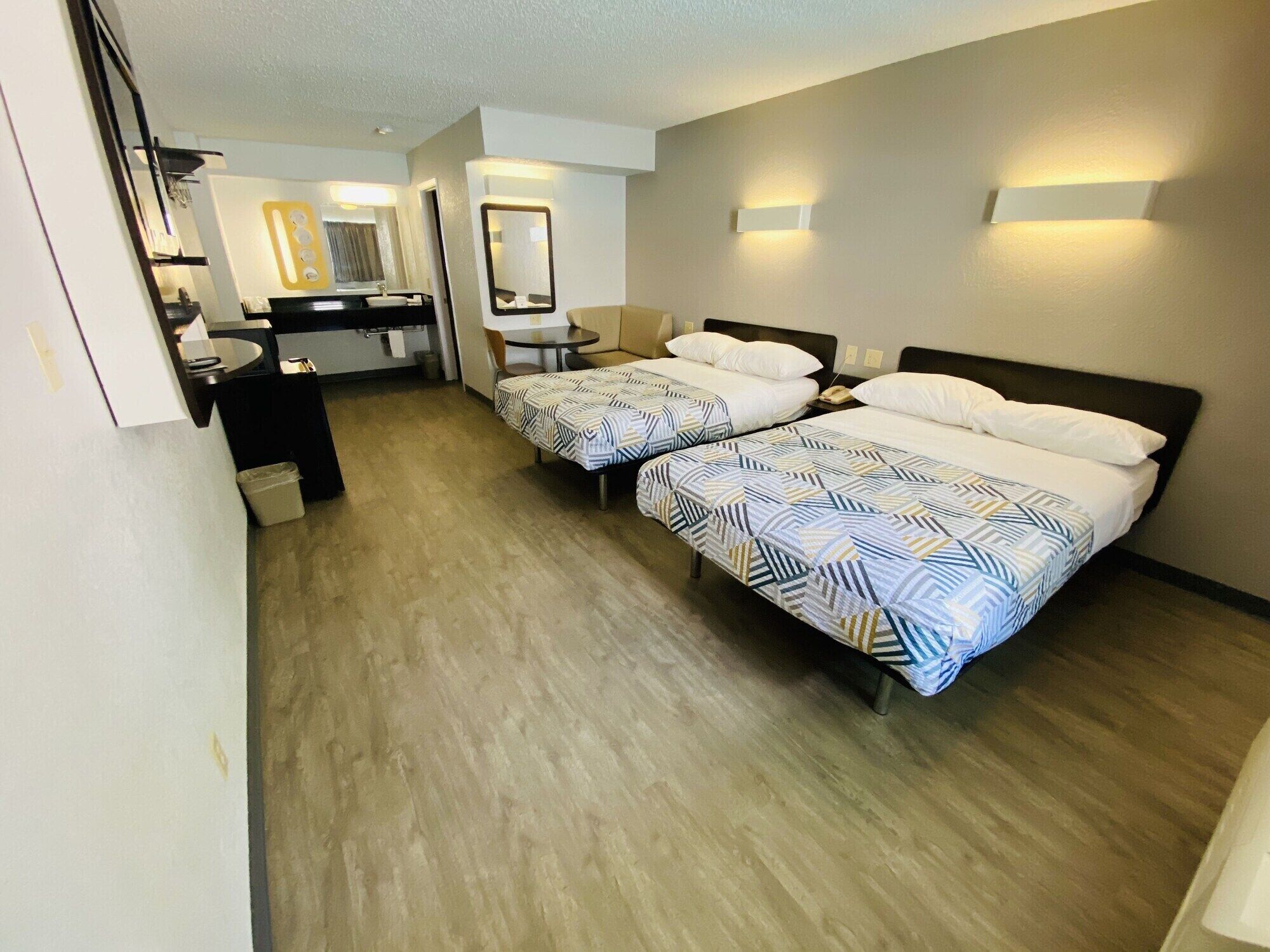 Habitación de hotel con dos camas, un escritorio, una silla y una kitchenette pequeña.