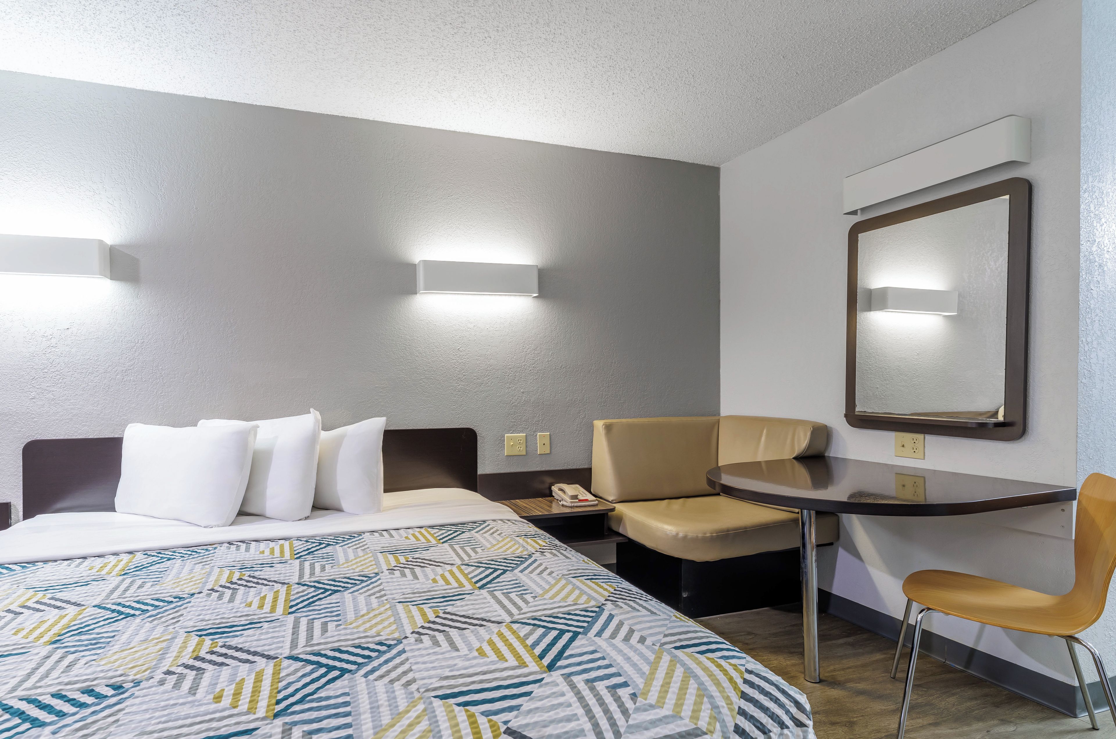 A hotel room with a bed, a desk, a chair, and a mirror.