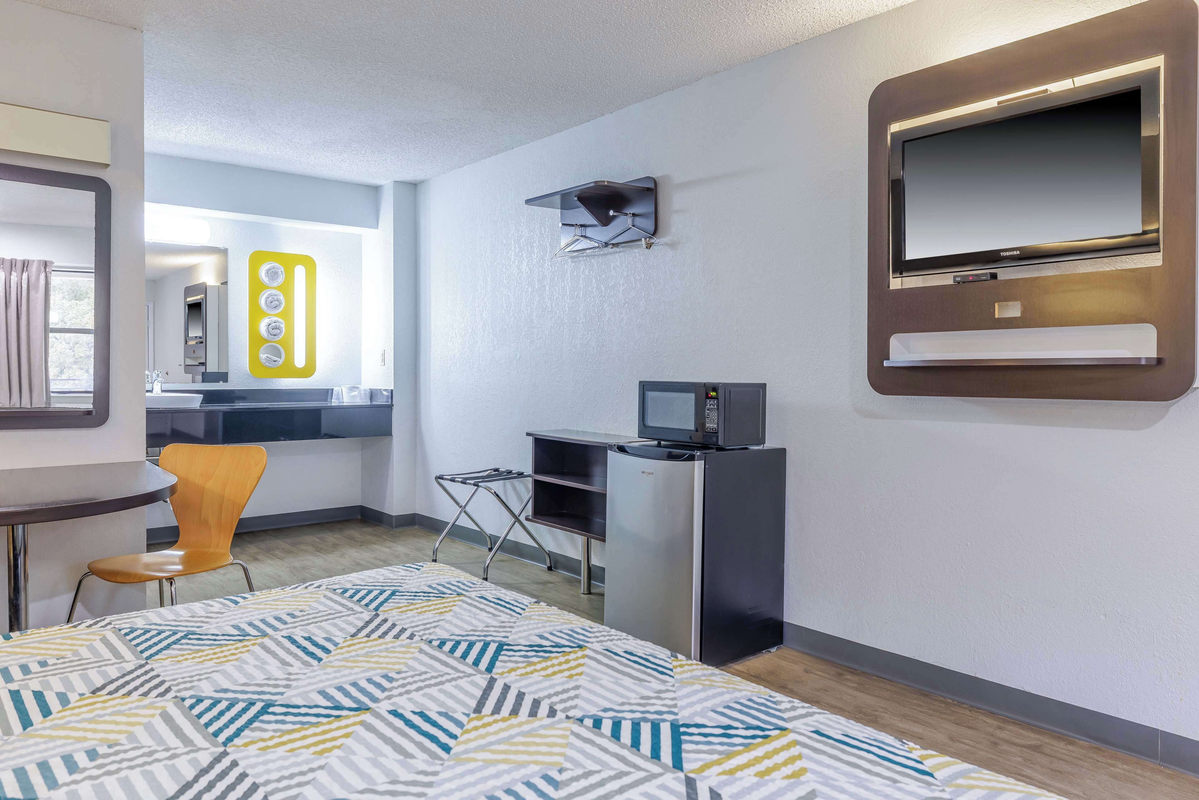 Een hotelkamer met een bed, bureau, stoel, televisie en een kleine kitchenette.
