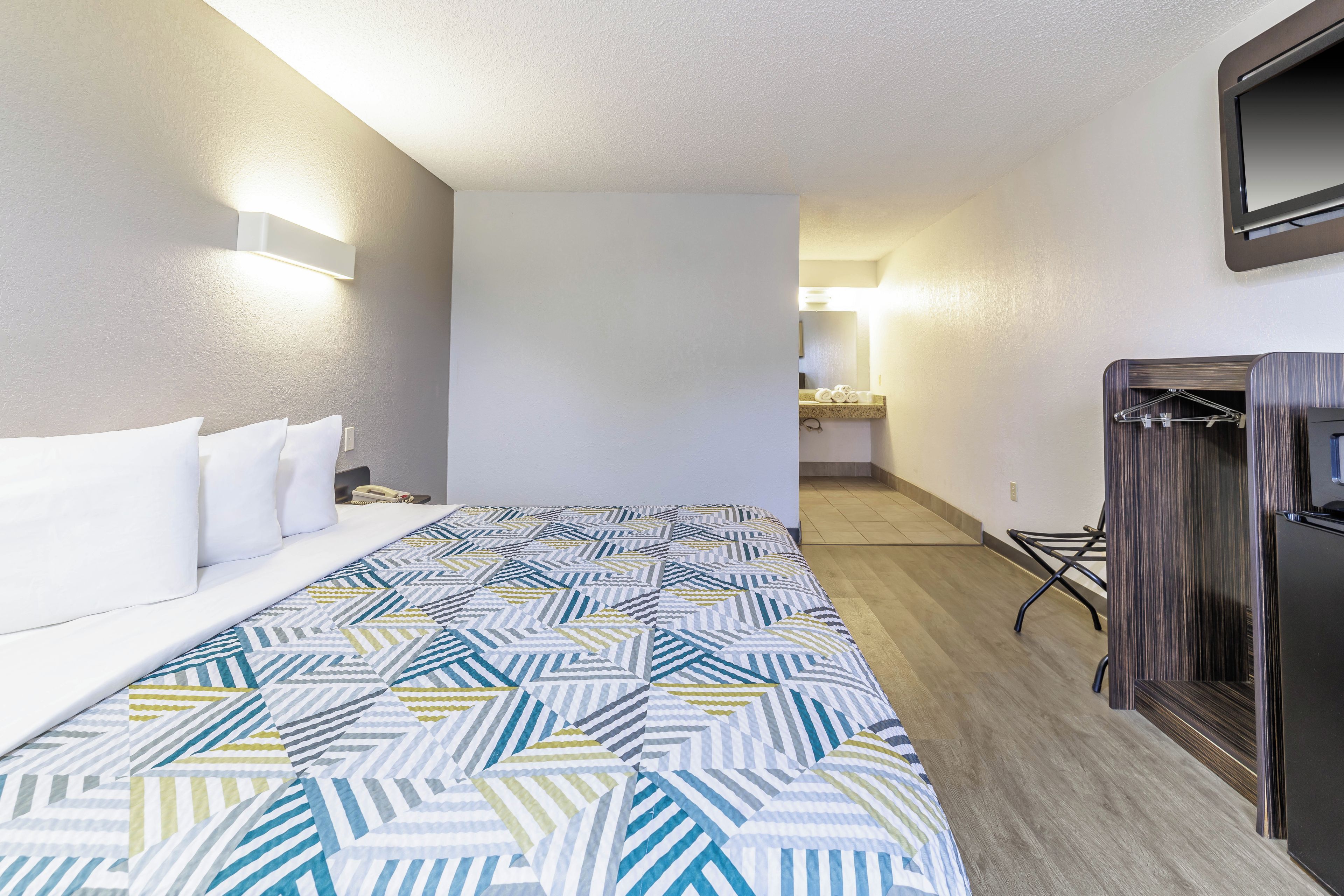 Una camera d'hotel con un letto, un comodino con il telefono, uno specchio e un armadio.