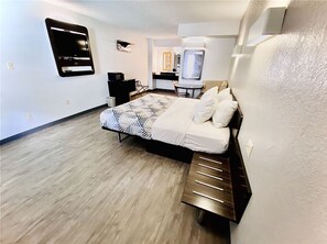 A modern hotel room with a bed, bedside table, and a small desk with a chair.