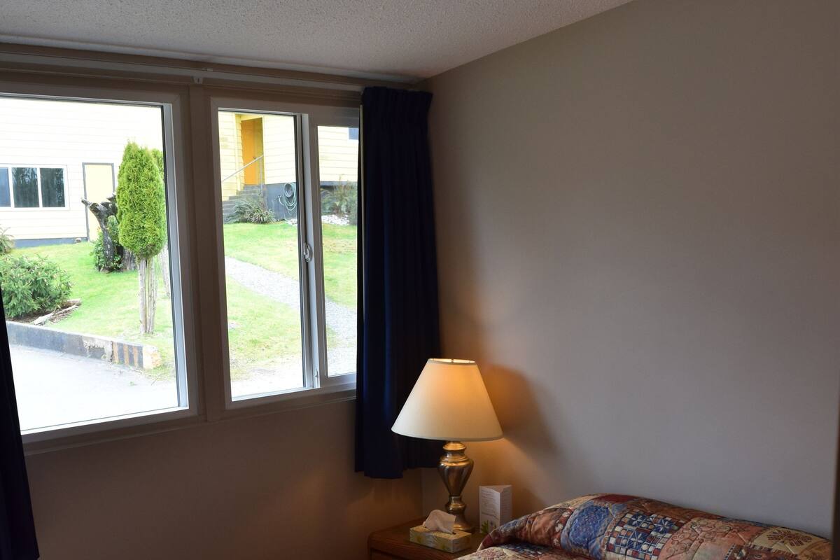 A room with a bed, a window, a lamp, and a view of the outside.