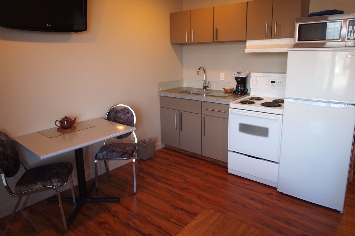 A compact kitchen with a dining table, chairs, a microwave, a stove, and cabinets.