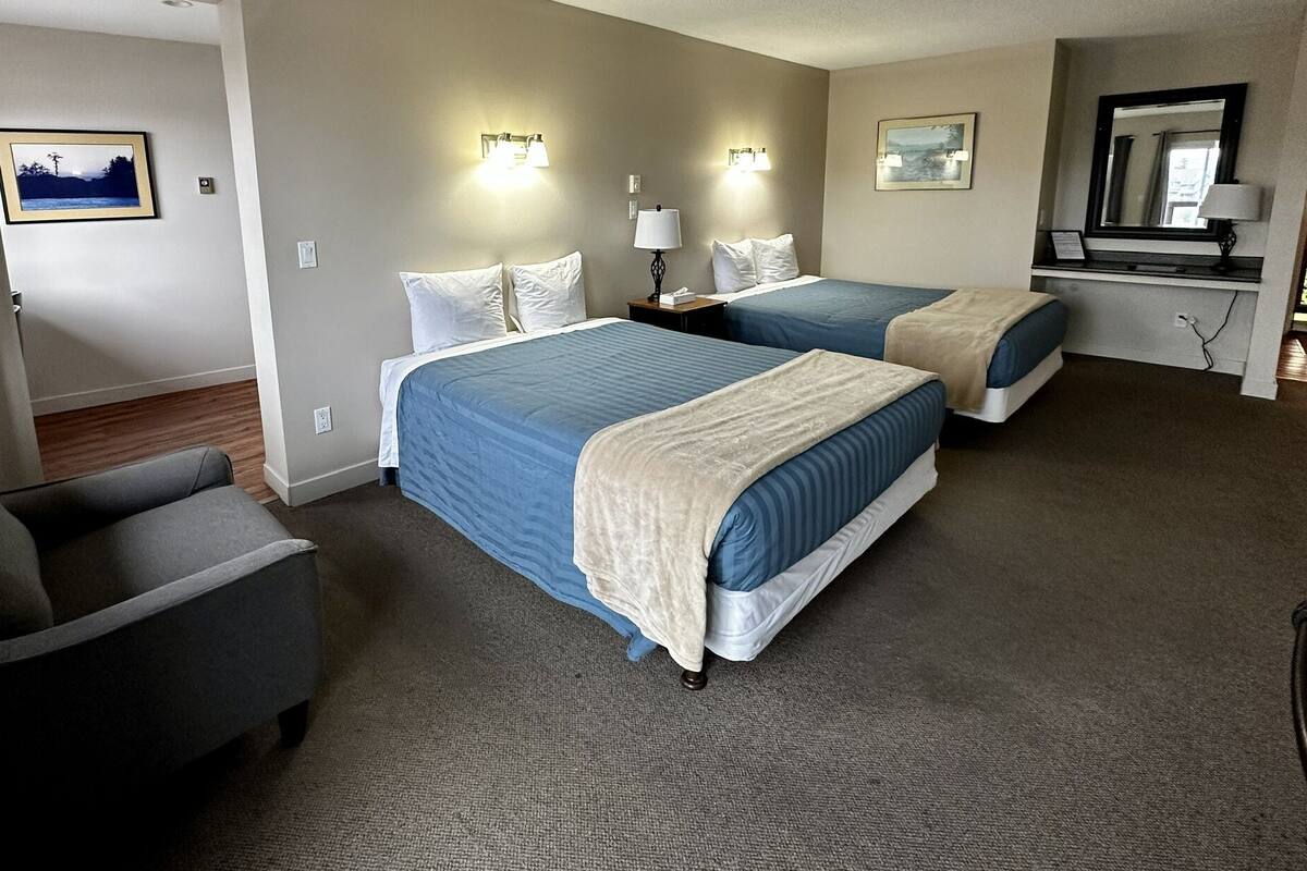 A hotel room with two beds, a chair, and a desk with a lamp.