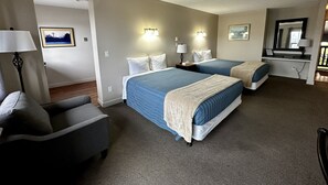 A hotel room with two beds, a chair, and a desk with a lamp. - West Coast Motel (Ucluelet)