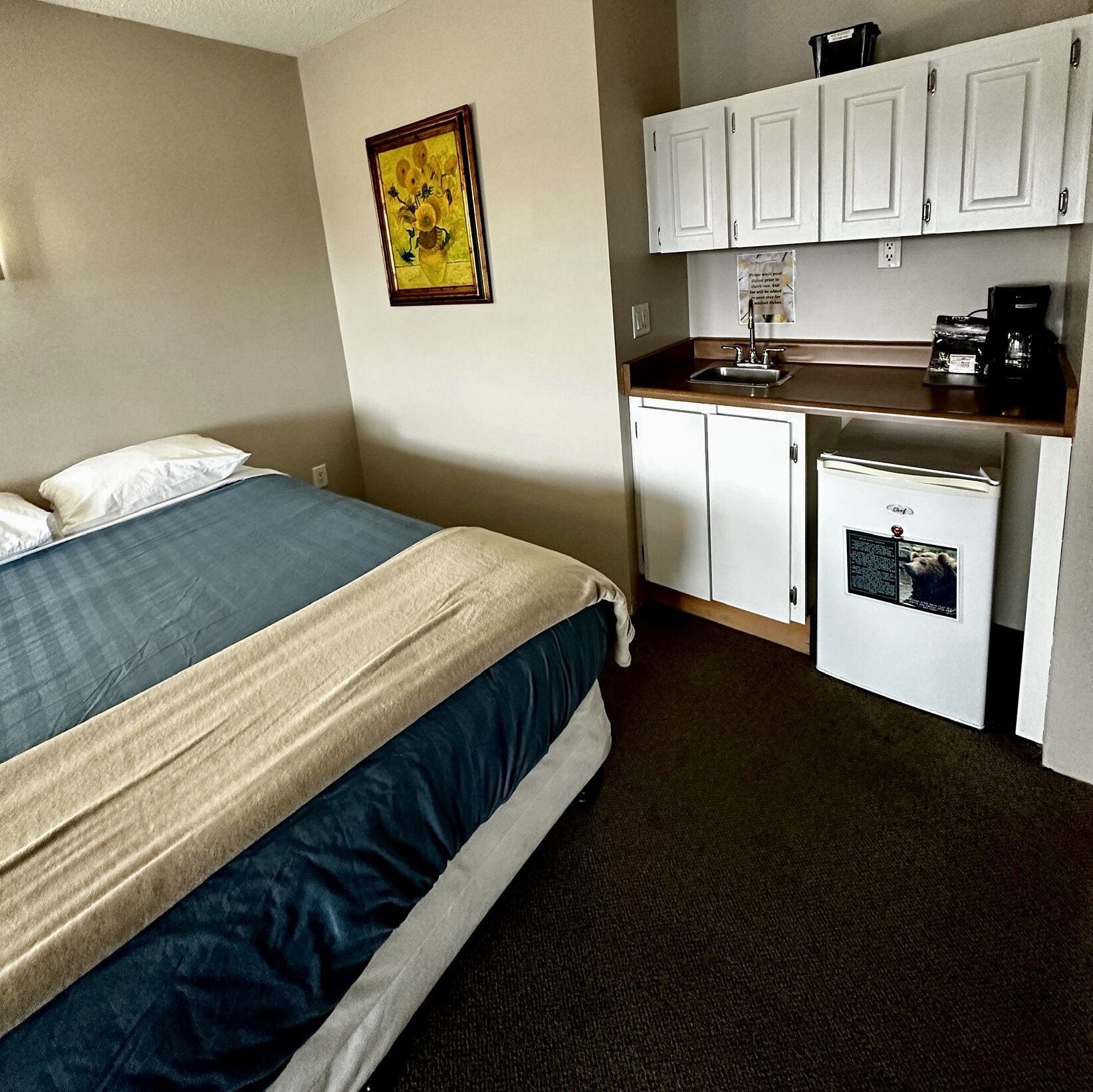 Un dormitorio con cama, una kitchenette con refrigerador y un cuadro colgado en la pared.