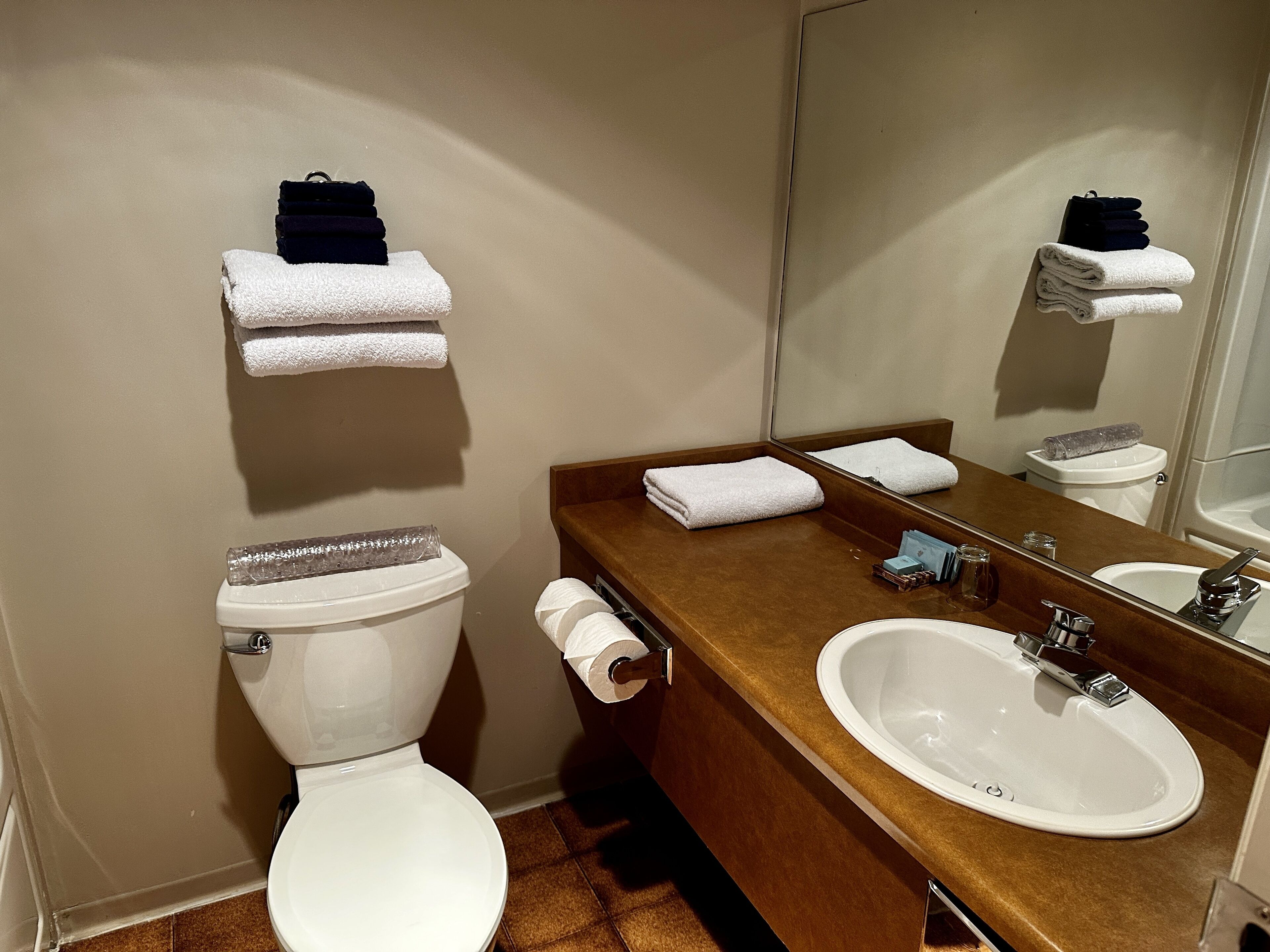 A bathroom with a toilet, sink, and mirror. There are towels and toiletries on the counter.