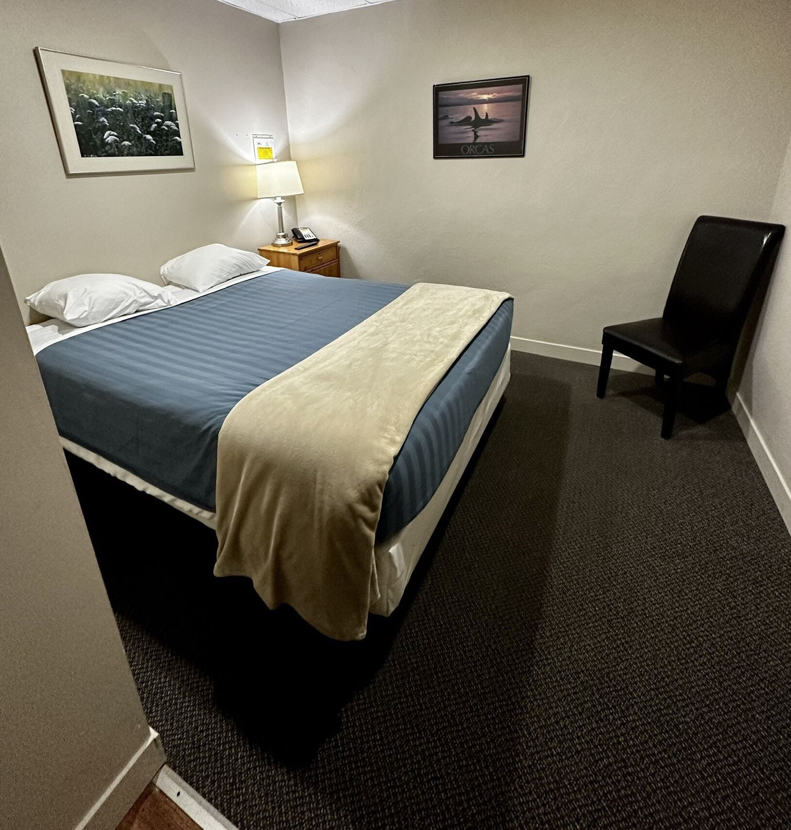 Een hotelkamer met een bed, een stoel, een lamp en twee foto's in lijsten aan de muur.