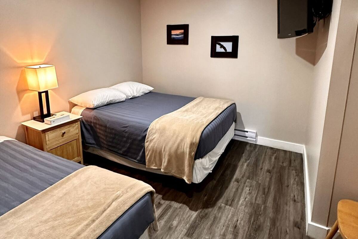 A hotel room with two beds, a nightstand with a lamp, a TV mounted on the wall, and a small wooden chair.