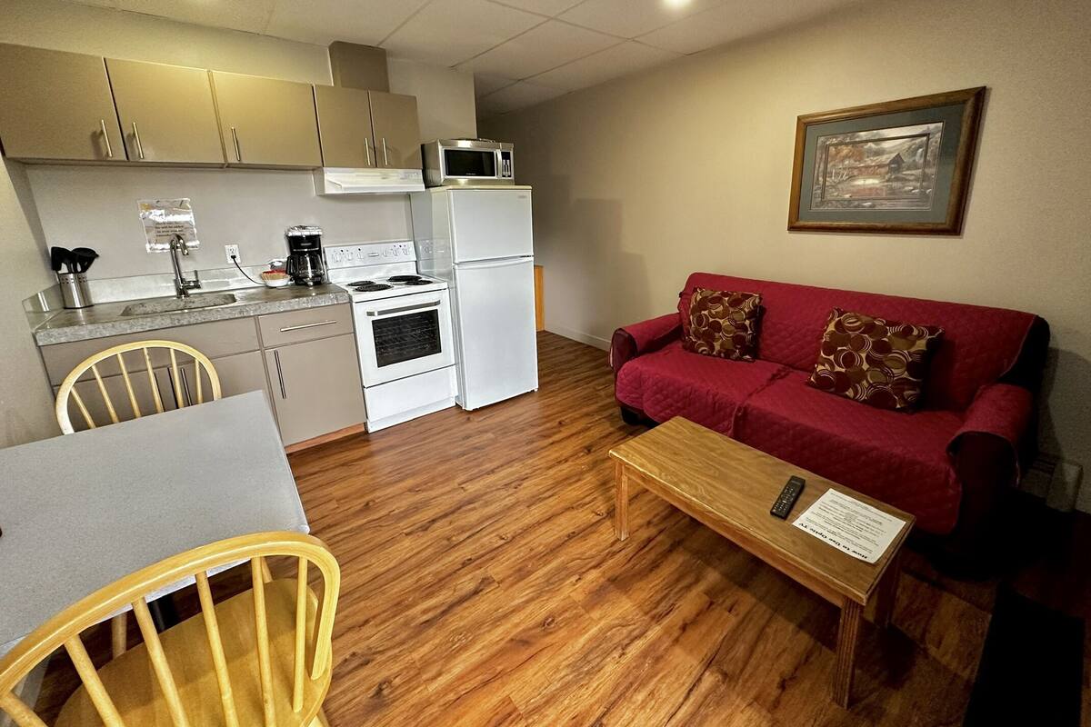 A compact living space with a kitchenette, a red sofa, a wooden coffee table, and a dining table with chairs.