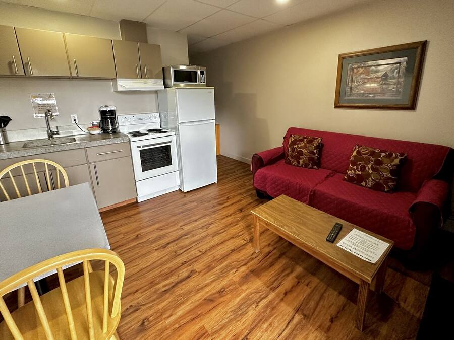 A compact living space with a kitchenette, a red sofa, a wooden coffee table, and a dining table with chairs.