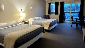 Habitación de hotel con dos camas, un escritorio y vistas al exterior.