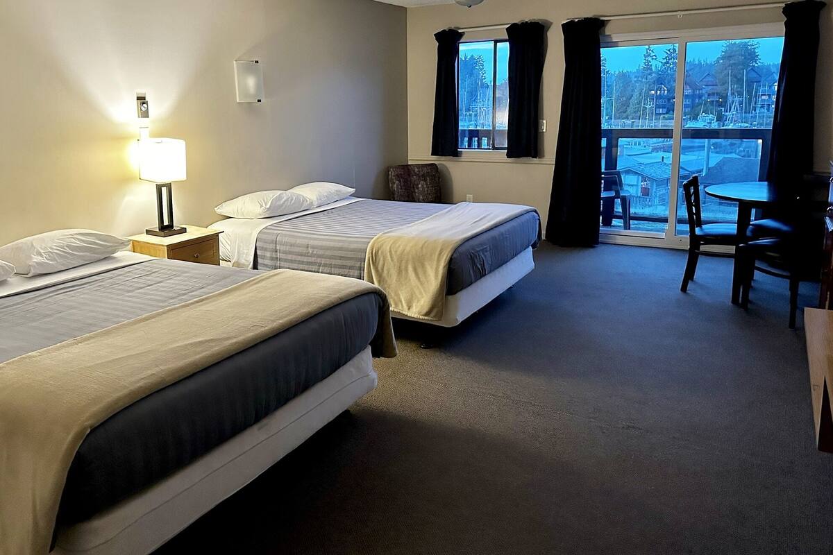 A hotel room with two beds, a desk, and a view of the outdoors.