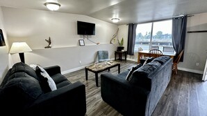 Una sala de estar con un sofá, un sillón, una mesa de centro y un televisor montado en la pared.