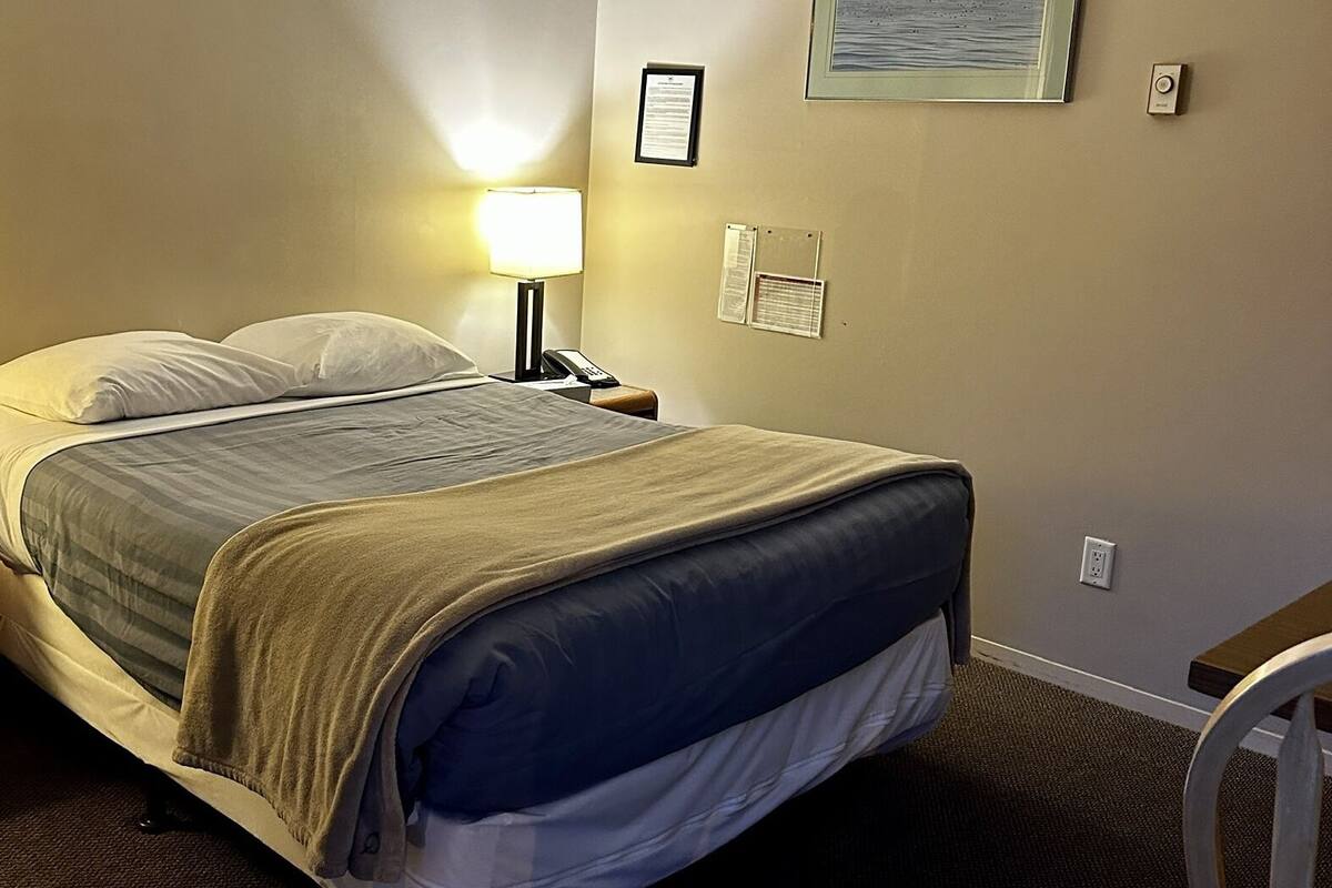 A hotel room with a bed, a nightstand with a lamp, a framed picture on the wall, and a chair.