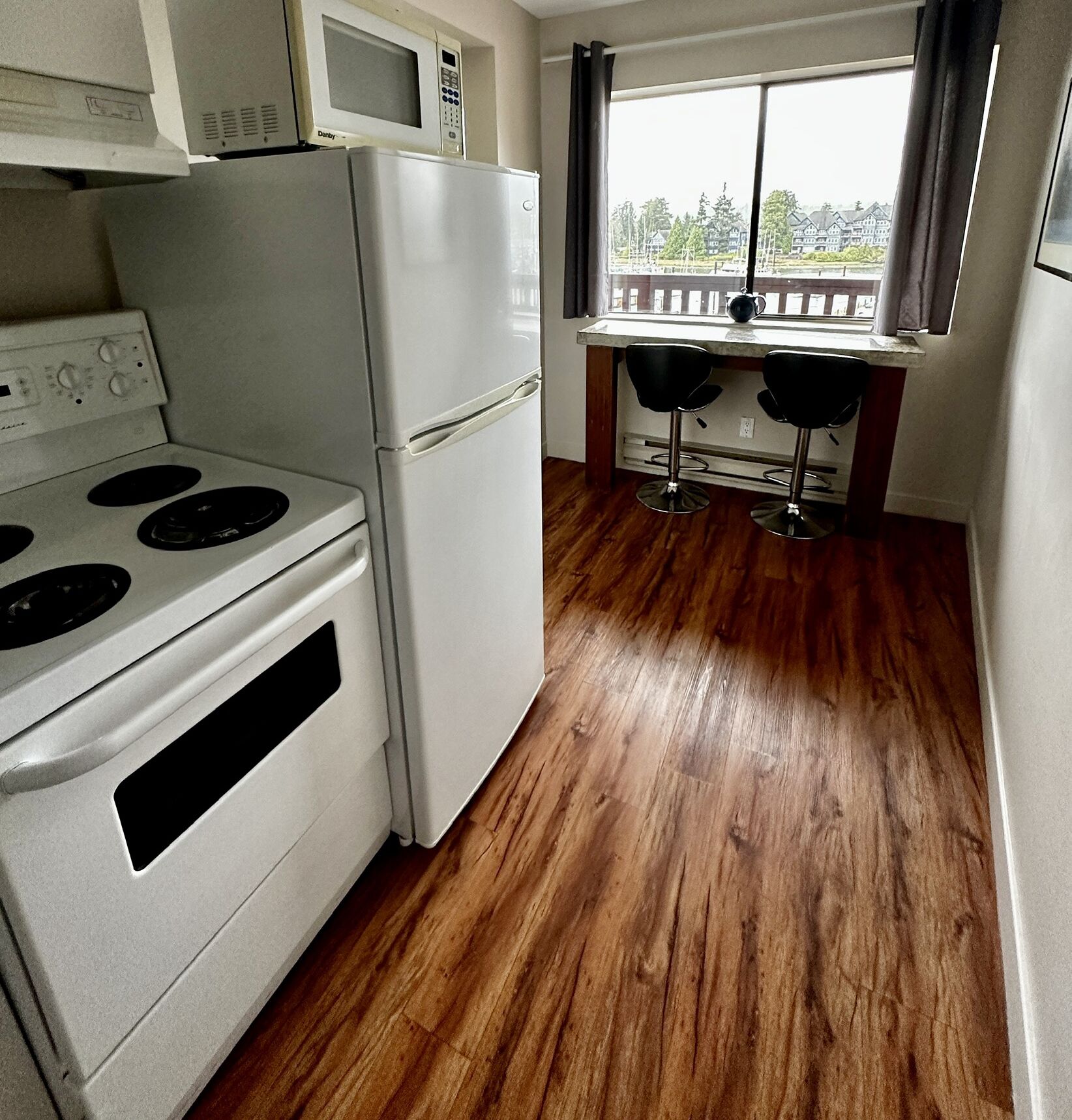 A compact kitchen with a stove, microwave, refrigerator, and two bar stools.