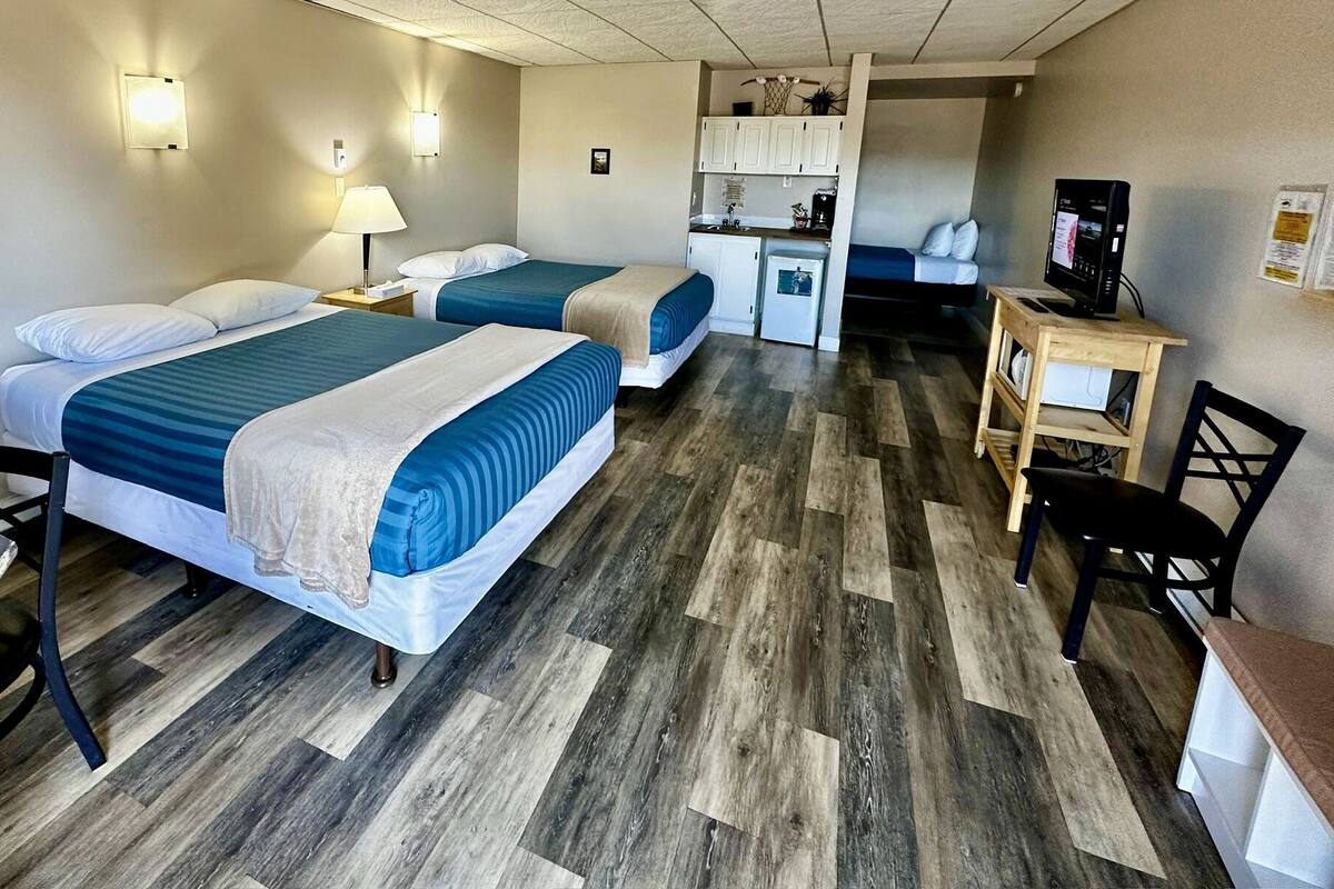 A hotel room with two beds, a desk, a chair, a kitchenette, and a TV.
