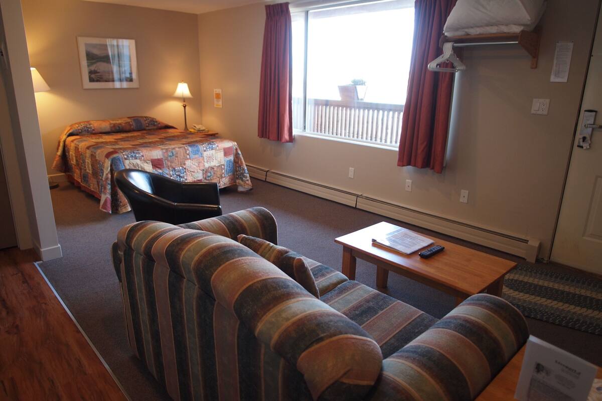 A hotel room with a bed, a sofa, a chair, a table, and a window with curtains.
