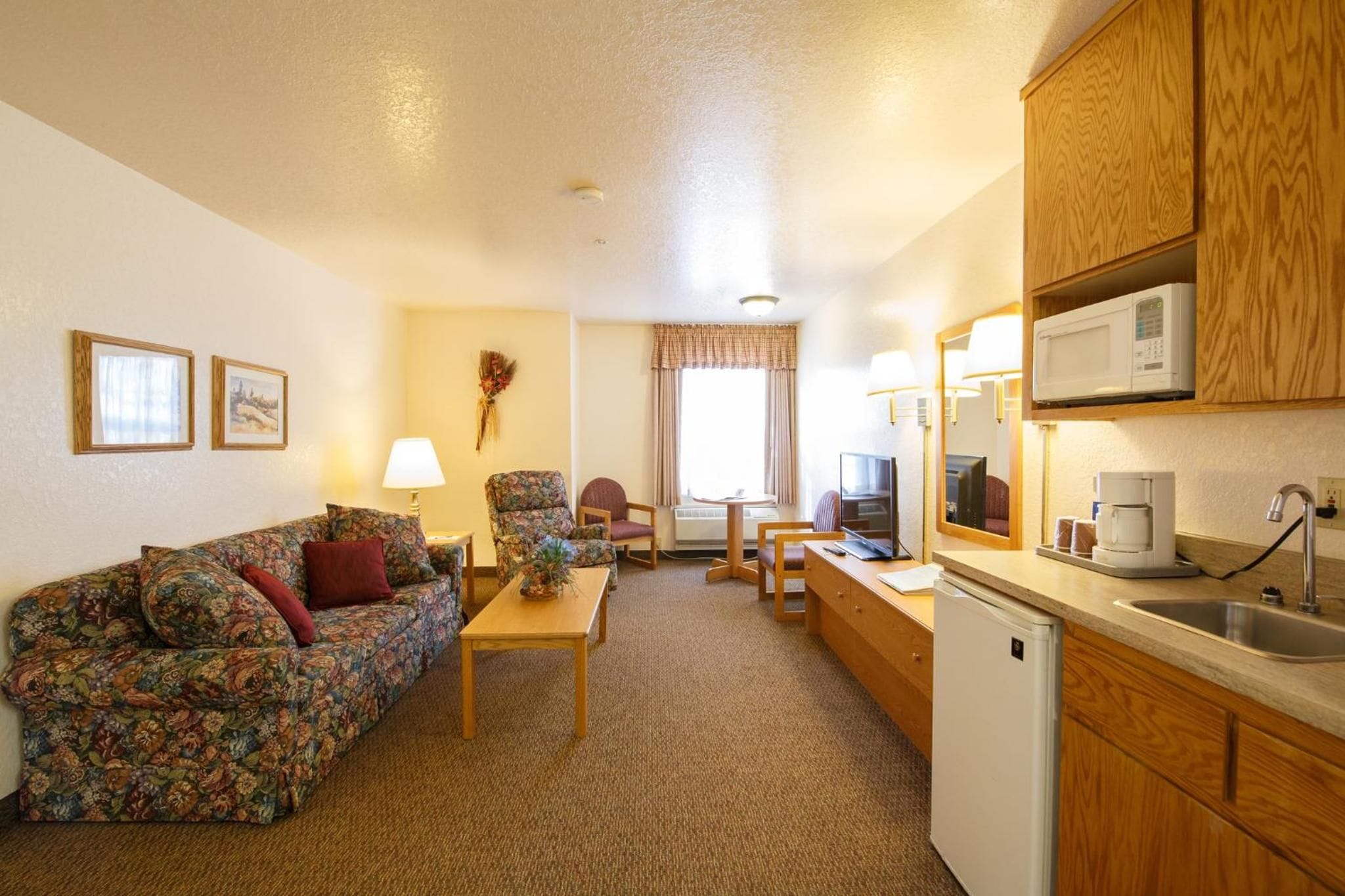 Un espacio habitable compacto con sofá, sillón, mesa de comedor, kitchenette y televisor.