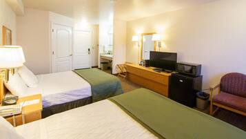 A hotel room with two beds, a desk with a television, a chair, and a small refrigerator.
