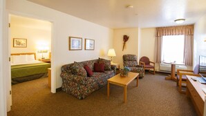 A hotel room with a bed, a floral sofa, a small table, a chair, and a desk with a computer.