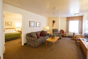 A hotel room with a bed, a floral sofa, a small table, a chair, and a desk with a computer.