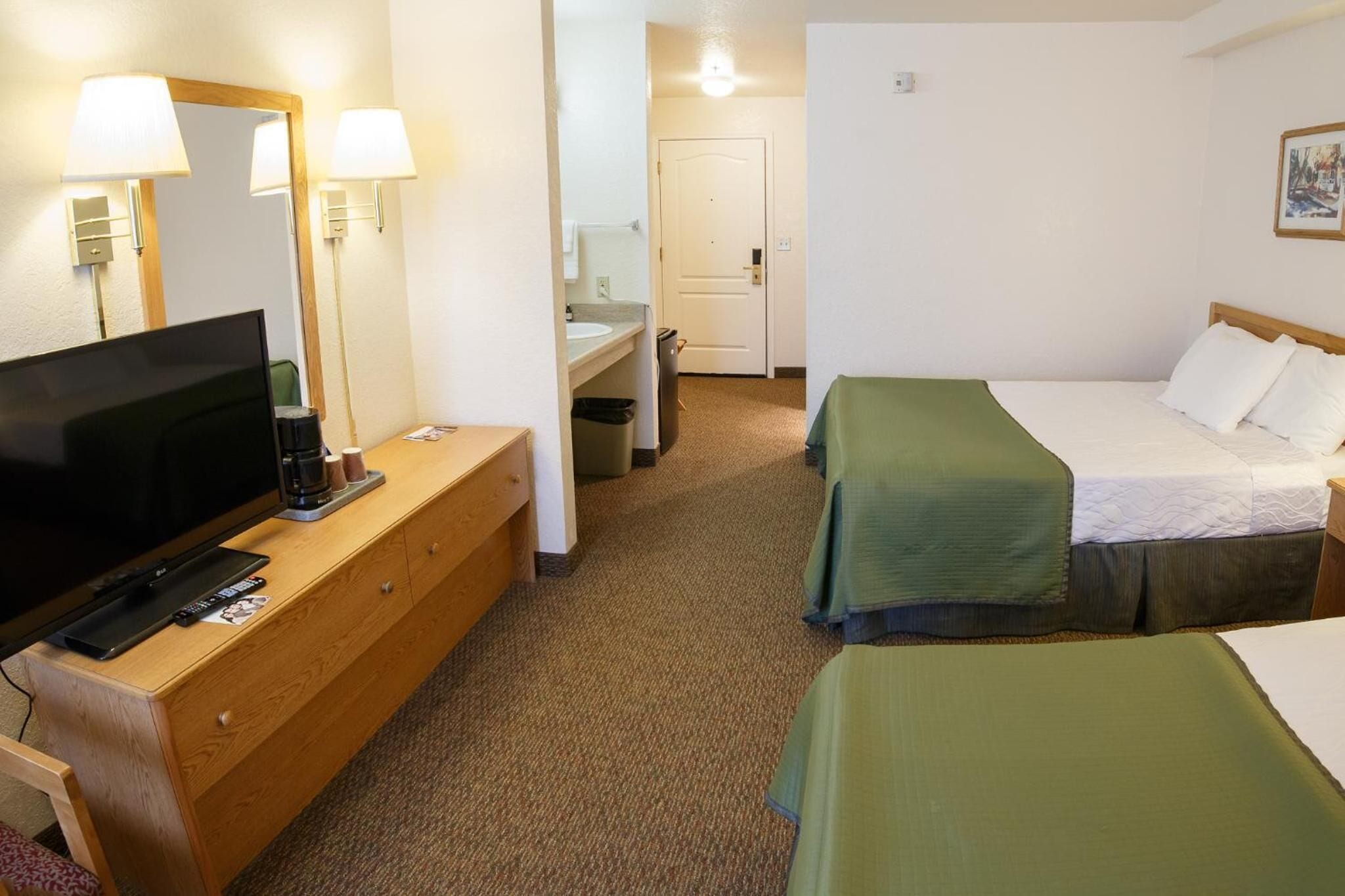 Une chambre d’hôtel équipée d’une télévision, d’une commode en bois, de deux lits, d’un miroir et d’une porte.