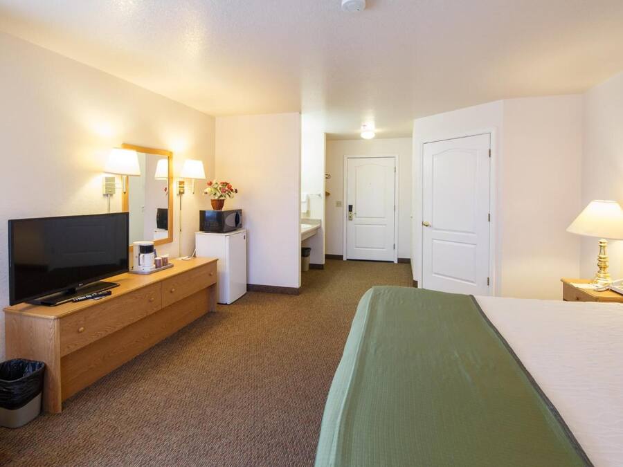Una habitación de hotel con cama, televisión, escritorio con computadora, lámpara y espejo.