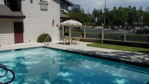 A swimming pool with a chair and umbrella, a small fence, and a building in the background. - Murphys Inn Motel (Murphys)