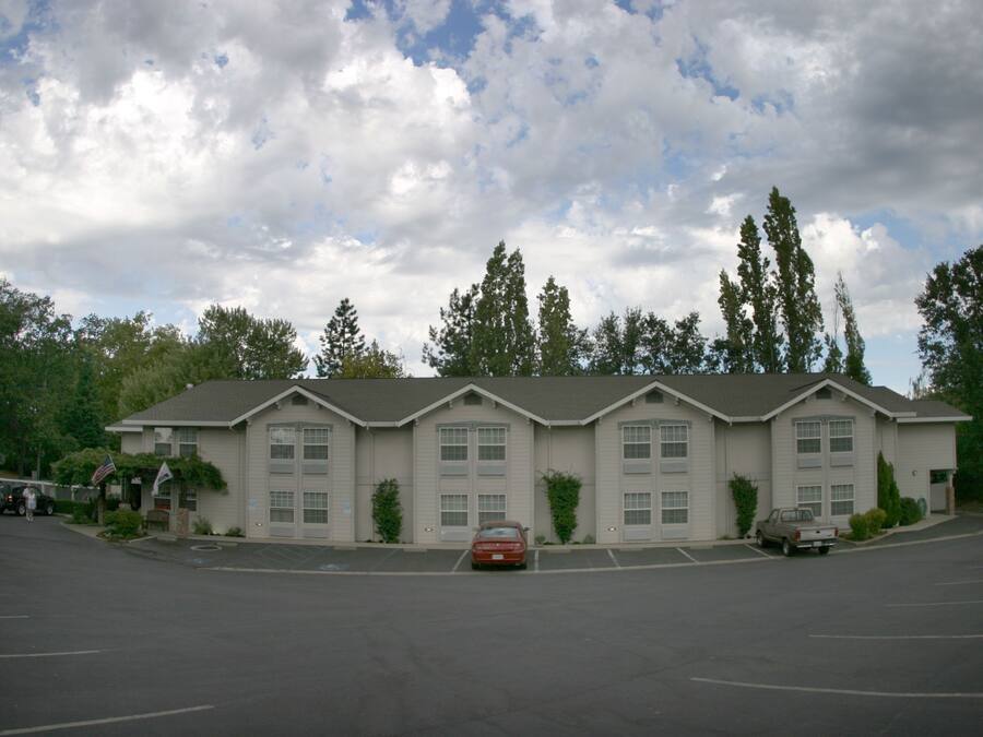 A motel with a parking lot, multiple buildings, and trees in the background.