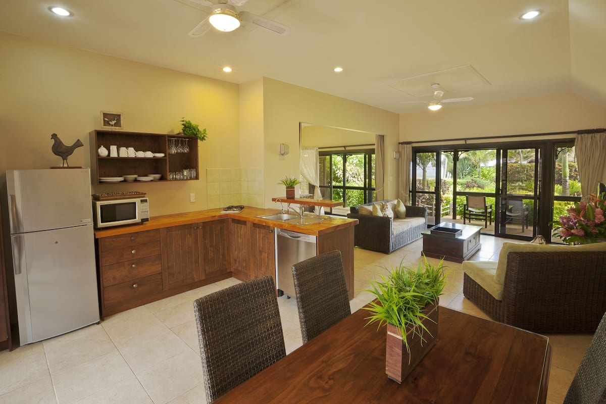A modern kitchen with a built-in microwave, wooden cabinets, and a dining area with wicker furniture.