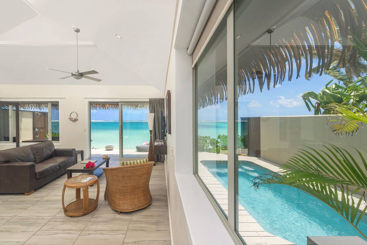 A modern living room with a large glass wall, a ceiling fan, a pool, and a view of the ocean.