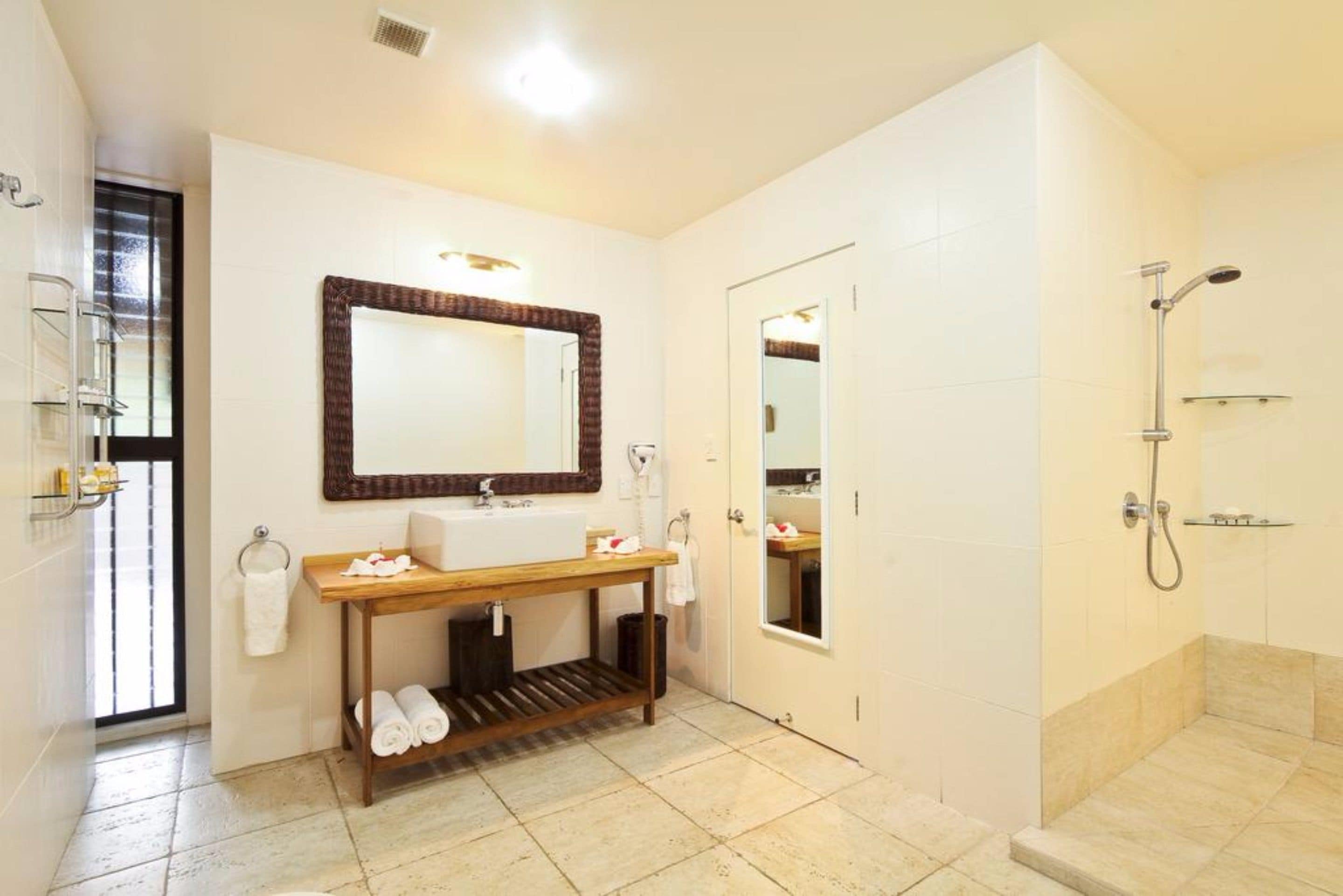 A modern bathroom with a large mirror, a sink, a wooden vanity, and a walk-in shower.