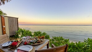 A wooden deck with a table set for a meal, overlooking a calm sea and a clear sky. - Sea Change Villas (Rarotonga)