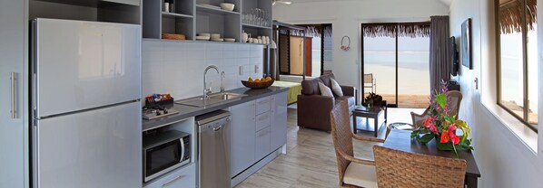 A modern kitchen with a dishwasher, oven, and microwave. There is a dining area with a table and chairs. - Sea Change Villas (Rarotonga)