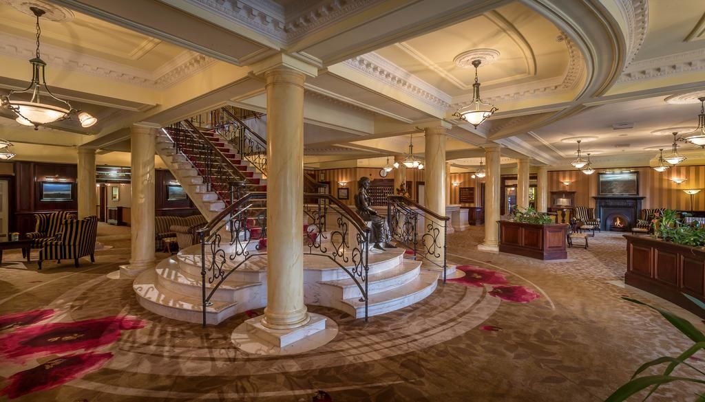 A grand lobby with a central staircase, large columns, and a fireplace.